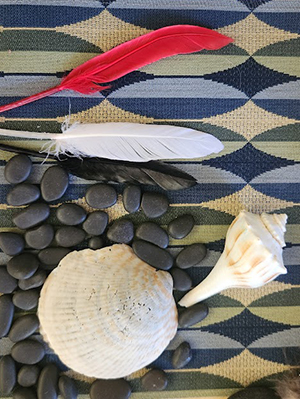 An arrangement of feathers, stones, and shells on a patterned mat