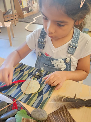 A young child arranges feathers, shells, stones, and sticks artistically