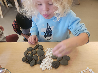 A young child arranges dark gray and white stones artistically