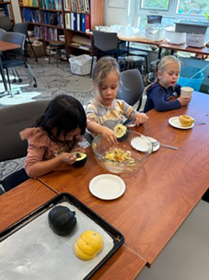 Three children scoop seeds from halved acorn squash and pumpkins before placing the squash on a baking tray