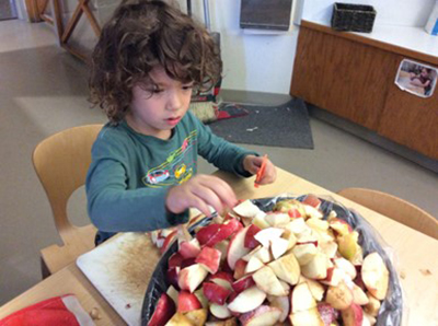 A child places apple slices in a slow cooker crock