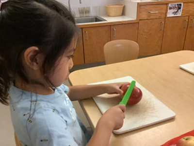 A child prepares to cut up an apple using a small green paring knife and cutting board